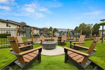 A set of four wooden chairs and a table are arranged around a fire pit.